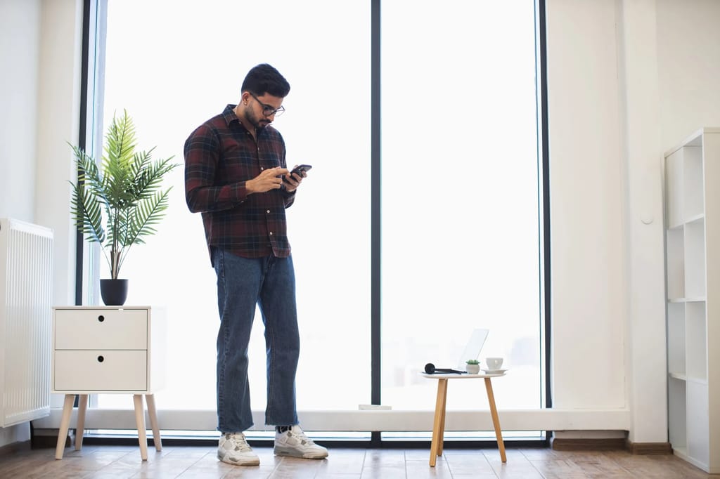 Mann mit Smartphone steht in Wohnzimmer