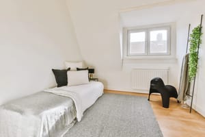 Comfortable bed with pillows, near a white wall in an attic bedroom with a window in a modern minimalist style